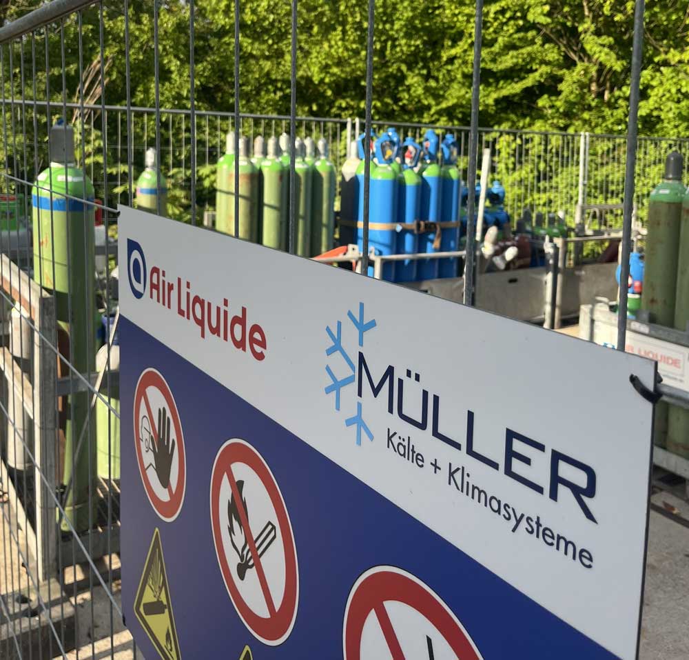 Ein Schild mit der Aufschrift "Müller" vor einem Zaun, umgeben von Rohren und weiteren Objekten.